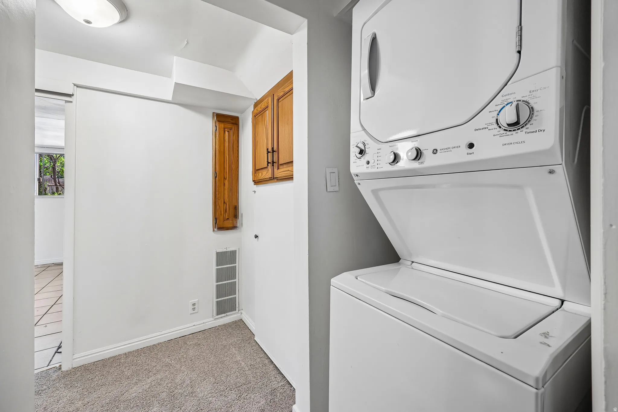 Dedicated laundry space featuring a stacked washer and dryer unit, overhead cabinetry, and carpeted flooring