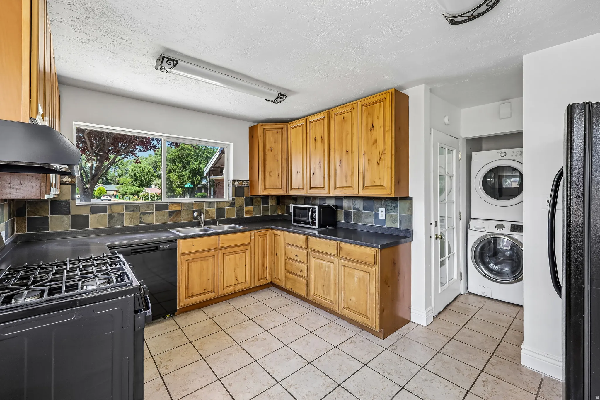 Kitchen featuring wood cabinetry, dark countertops, a tiled backsplash, and tile flooring