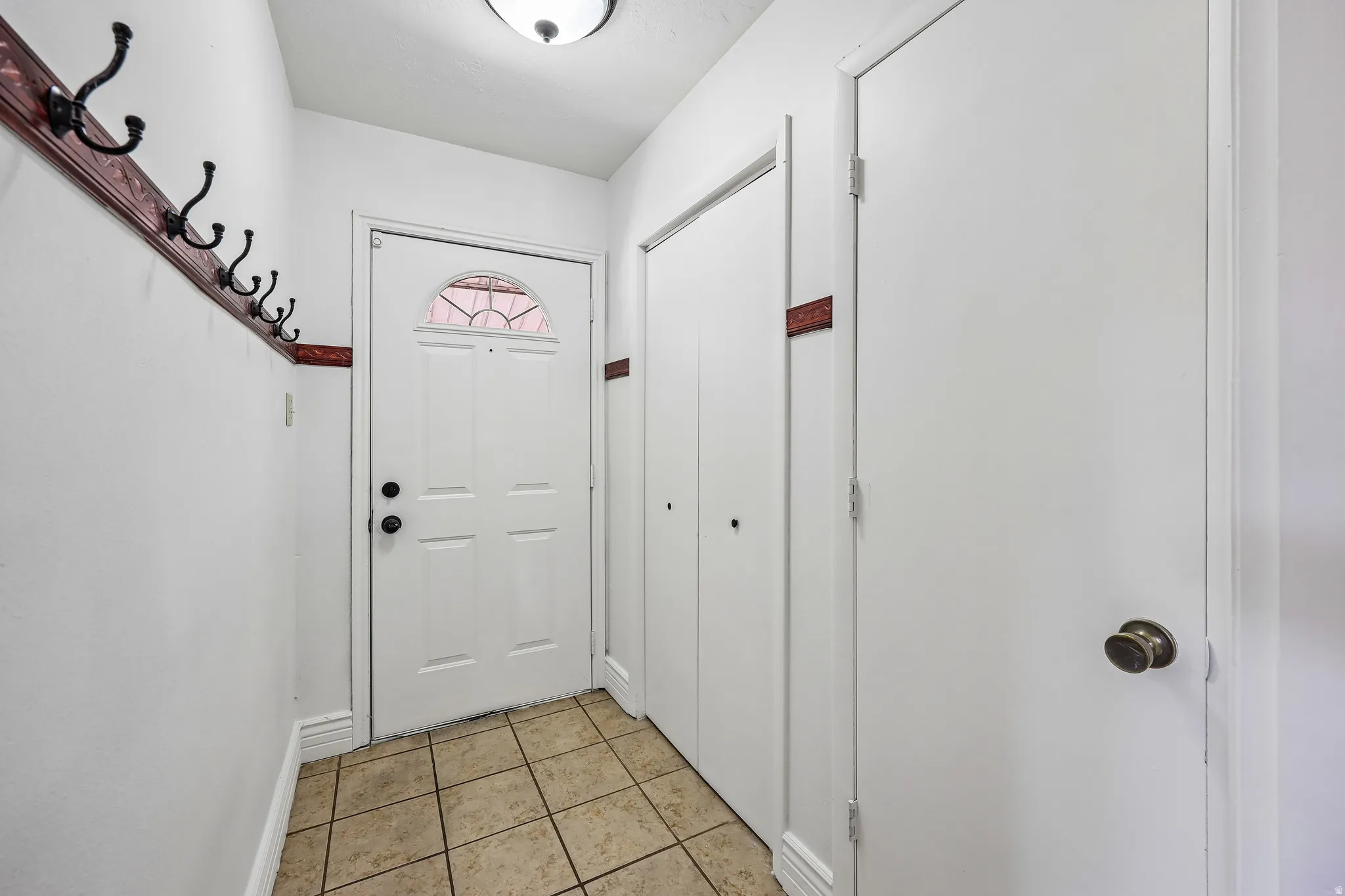 Entryway featuring ceramic tile flooring, a white paneled door with an arched window insert, and a wall-mounted coat rack
