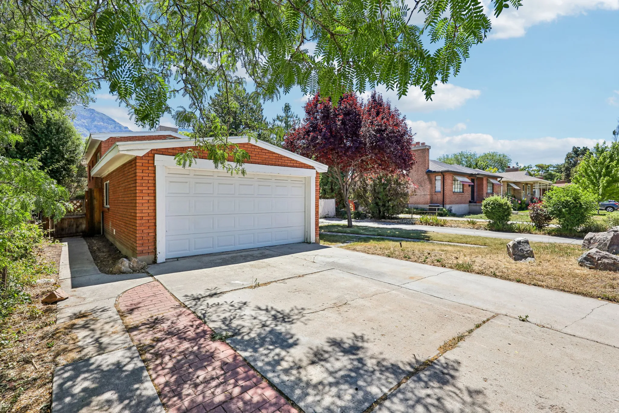 Brick exterior featuring an attached two-car garage with a white panel door, concrete driveway, and a red brick pathway