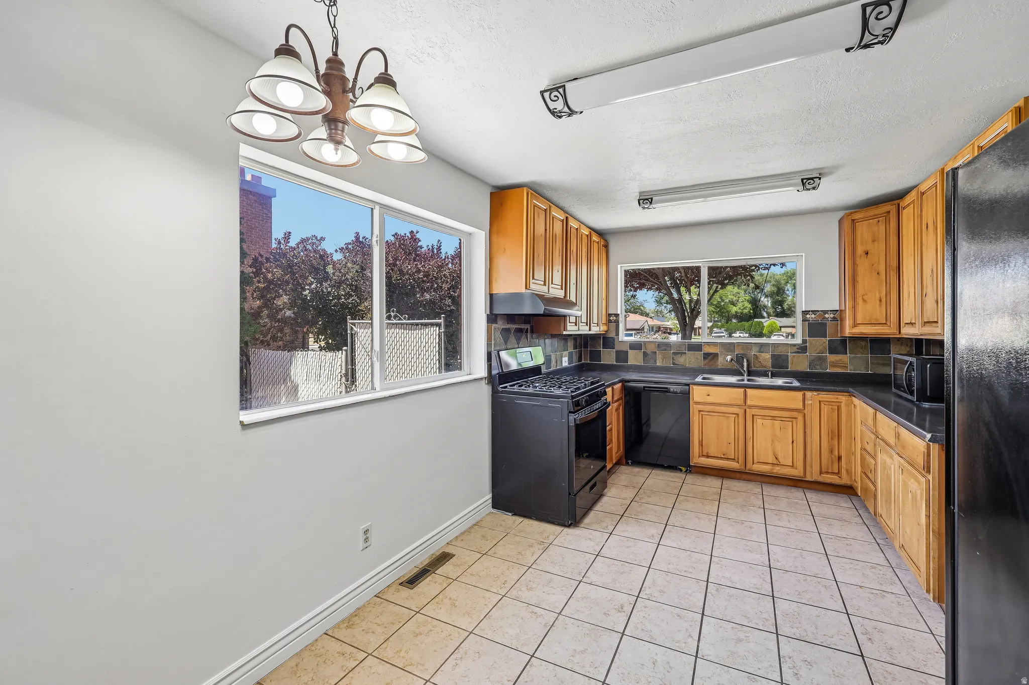 Kitchen featuring wood cabinetry, black appliances, tile flooring, and a multi-toned tile backsplash