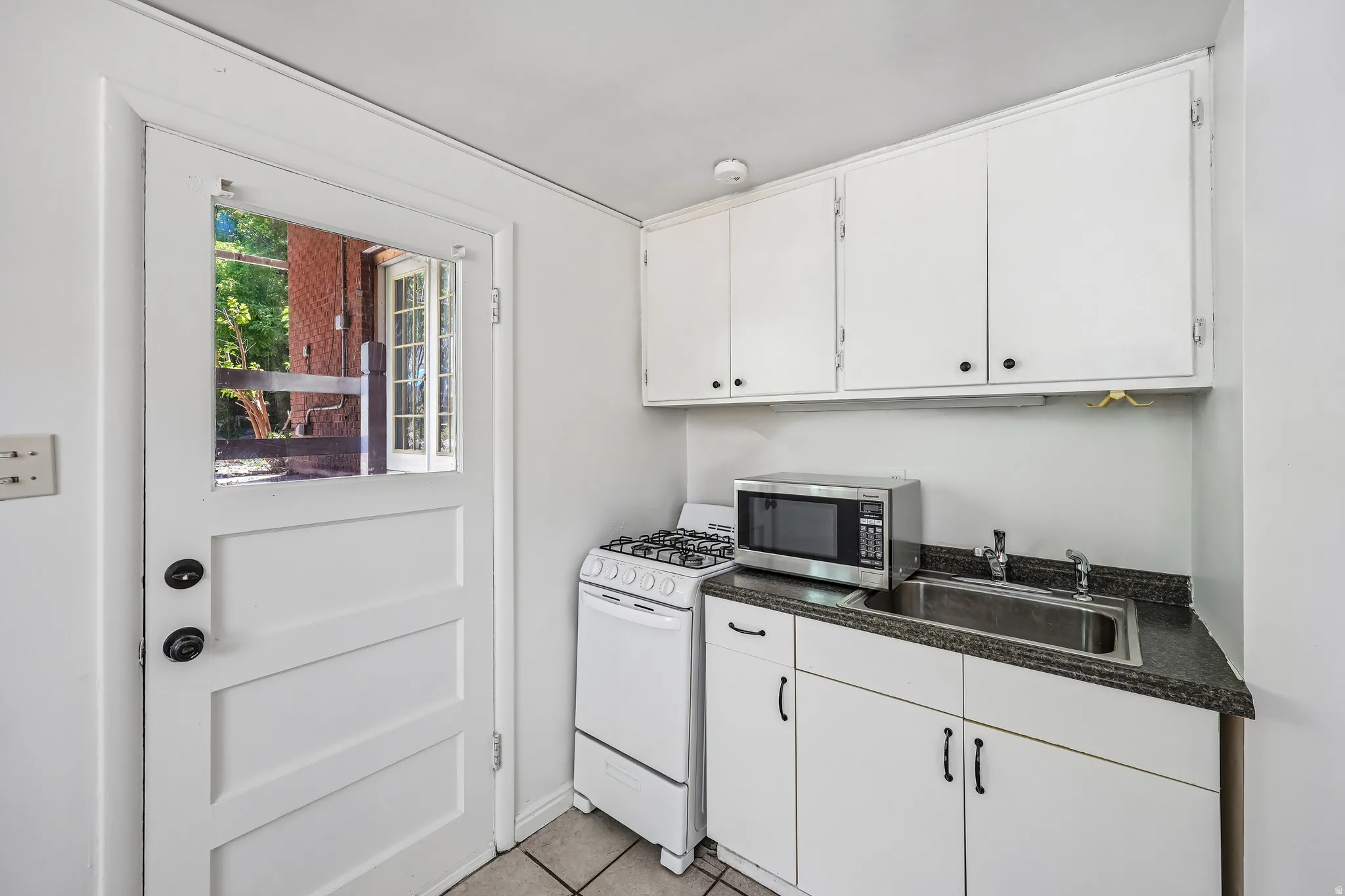 Compact kitchen space featuring white cabinetry, a stainless steel sink with coordinating faucet, and dark countertops