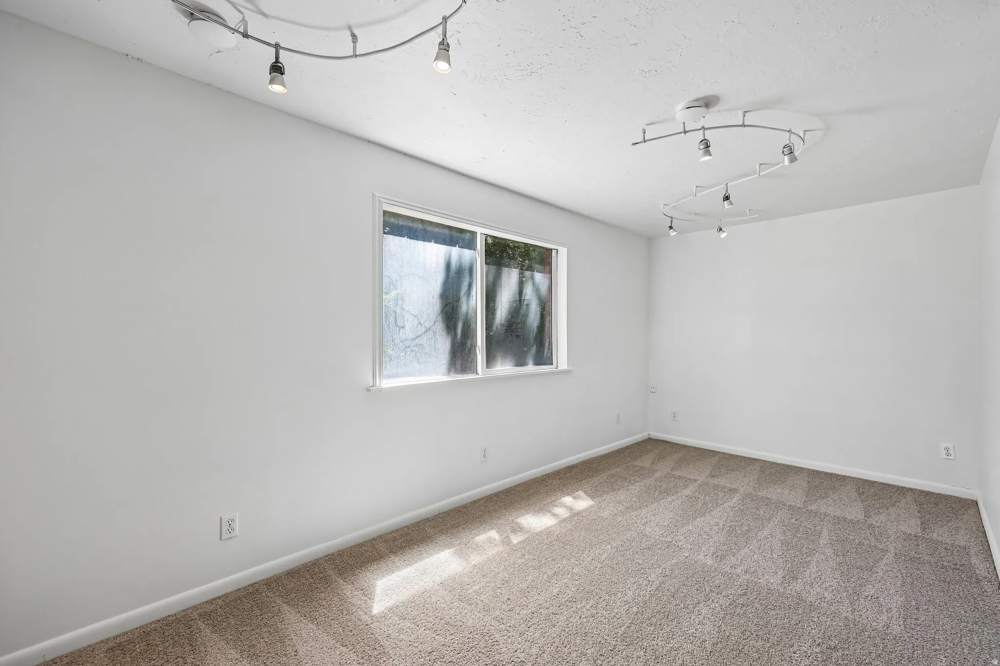 Room featuring light neutral-toned walls, track lighting, a window, and textured carpet flooring