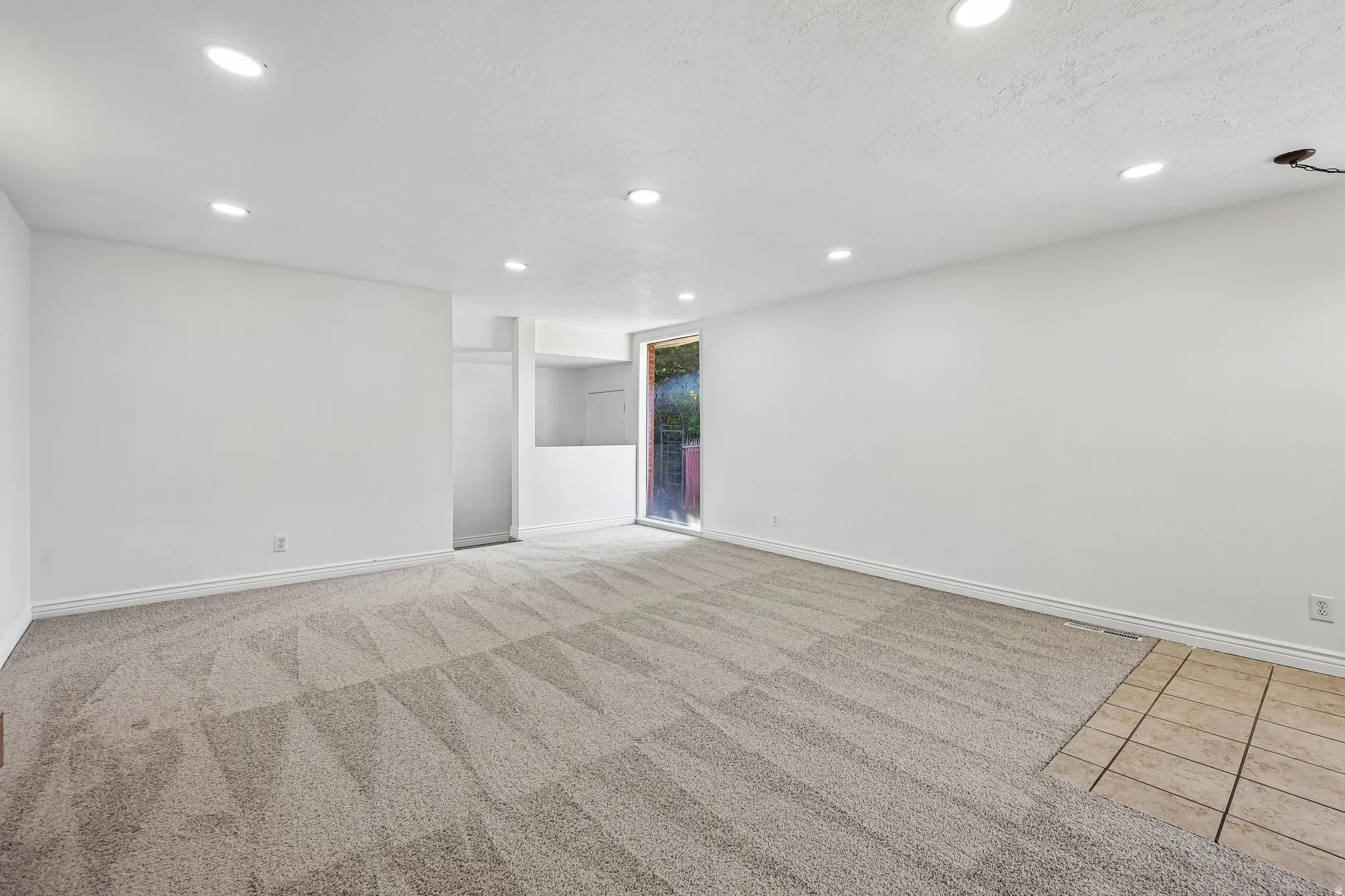 Spacious room featuring neutral carpeting, recessed lighting, white walls, and a sliding glass door