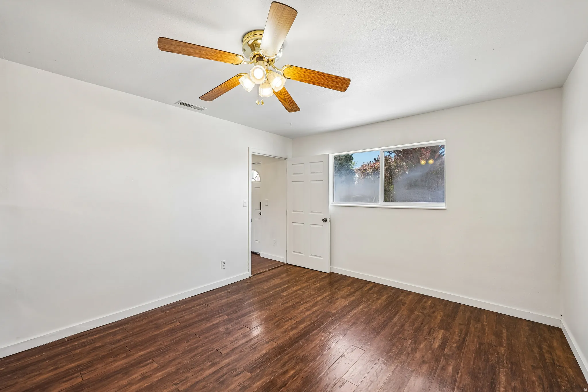 Spacious room featuring wood-finish flooring, white walls, and a ceiling fan with integrated lighting