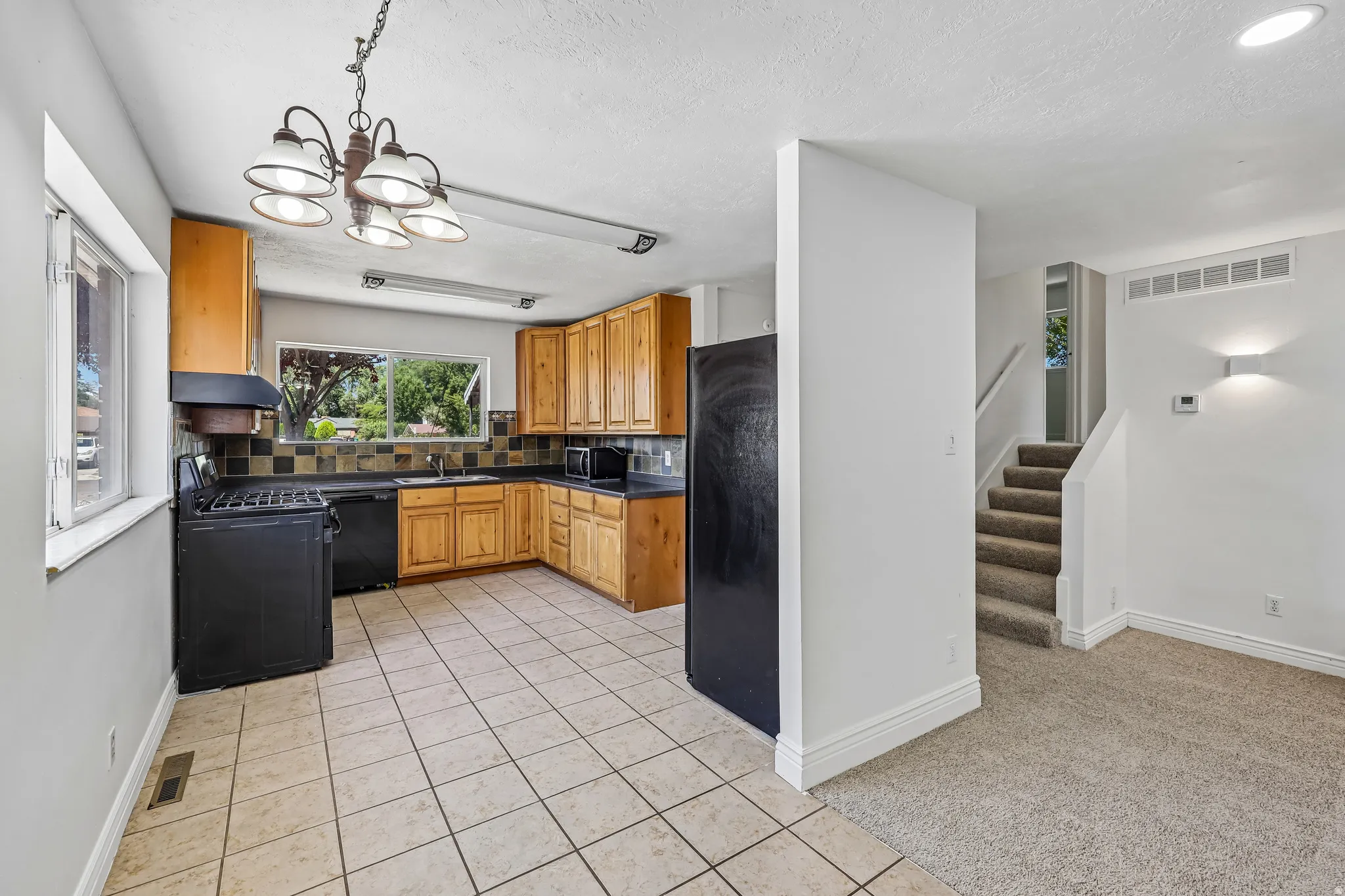 Kitchen featuring light wood cabinetry, black appliances, a black and beige tiled backsplash, and light-toned tile flooring