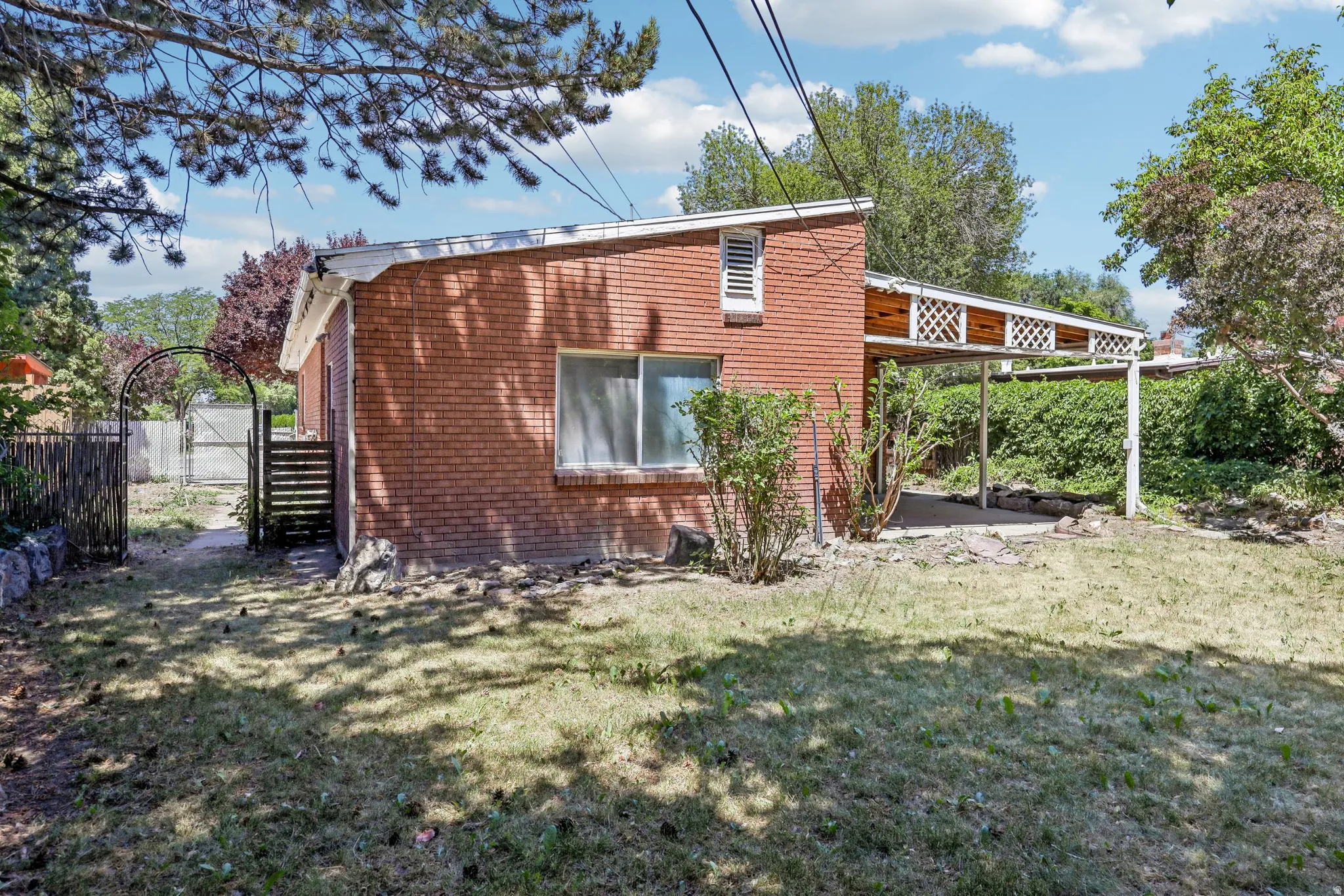 Brick exterior featuring a covered patio, a small window, and a white trellis detail