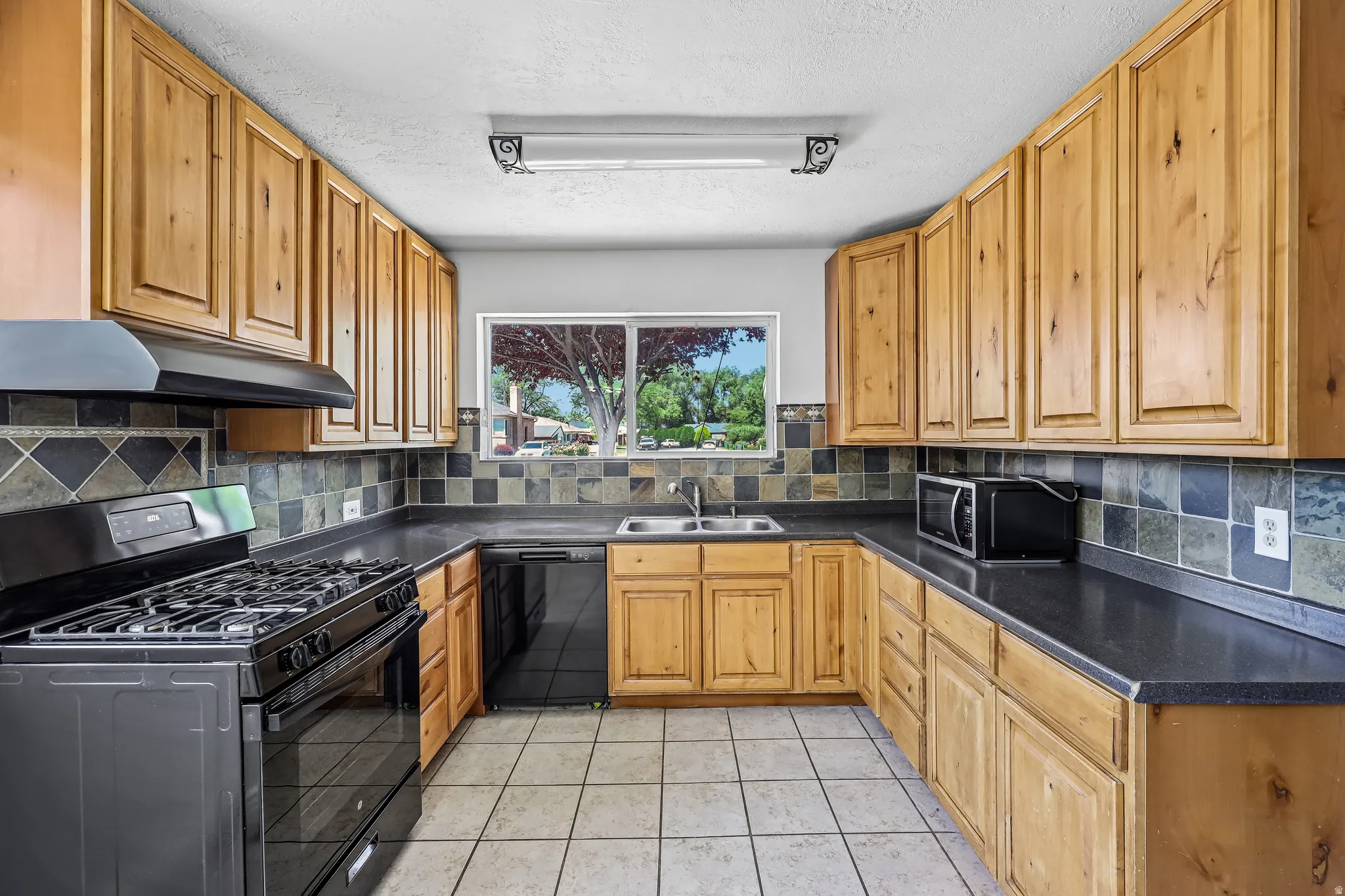 Kitchen featuring wood-finish cabinetry, dark countertops, and a full tile backsplash