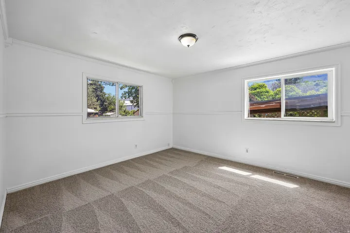 Spacious room featuring neutral carpet flooring, two large windows, white walls, and crown molding