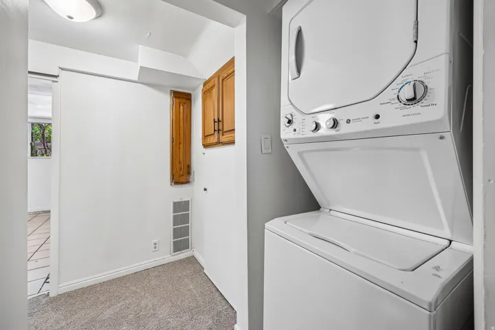Dedicated laundry space featuring a stacked washer and dryer unit, overhead cabinetry, and carpeted flooring