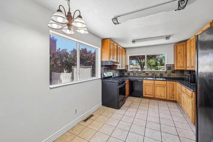 Kitchen featuring wood cabinetry, black appliances, tile flooring, and a multi-toned tile backsplash