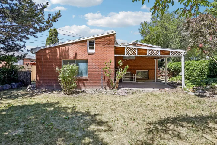 Brick exterior featuring an integrated covered patio with lattice detailing, a large window, and mature perimeter foliage