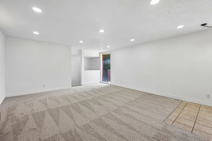 Spacious room featuring neutral carpeting, recessed lighting, white walls, and a sliding glass door