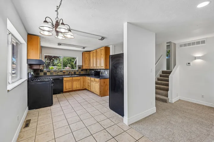 Kitchen featuring light wood cabinetry, black appliances, a black and beige tiled backsplash, and light-toned tile flooring