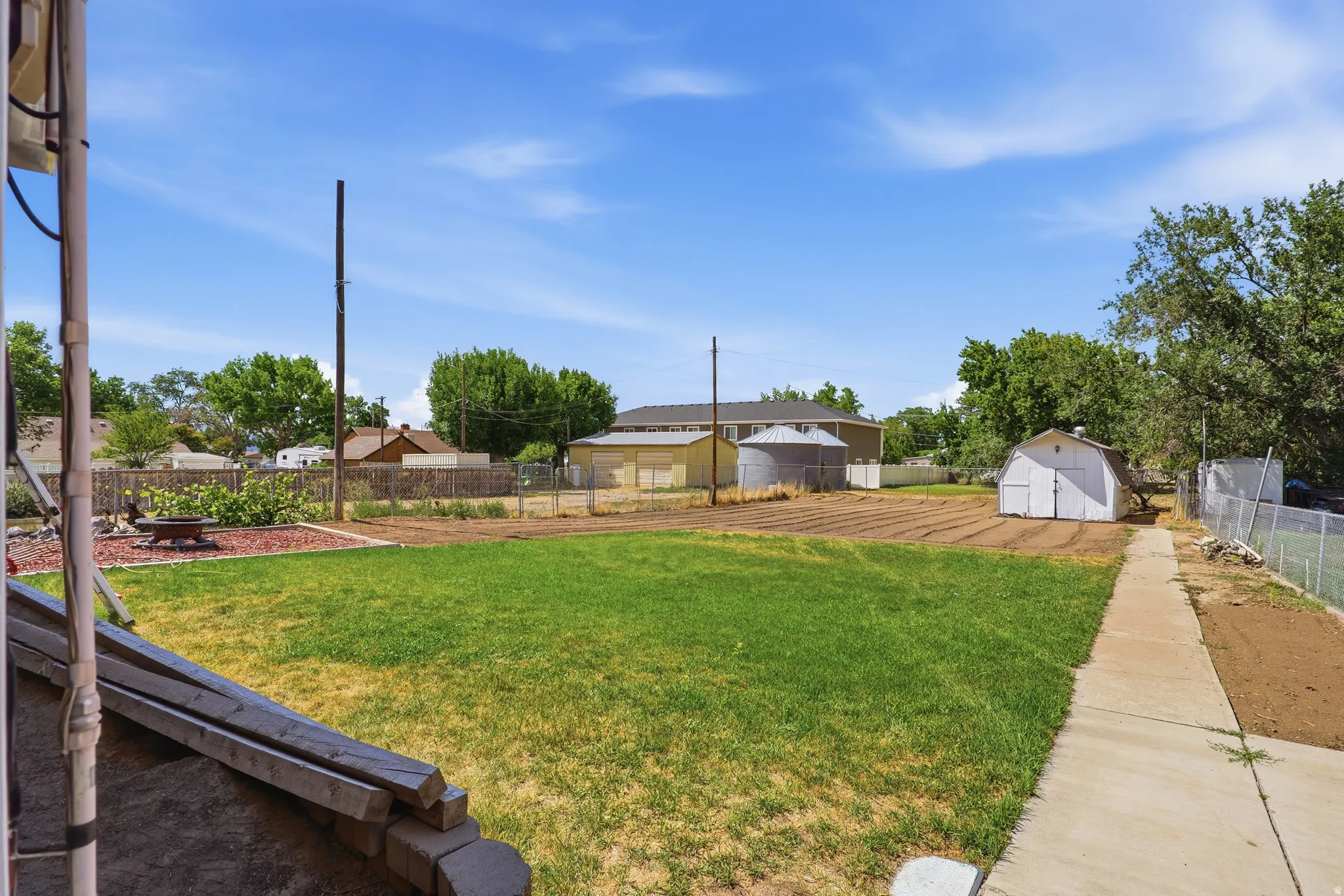 Expansive backyard featuring a large lawn, dedicated garden area, and a white storage shed