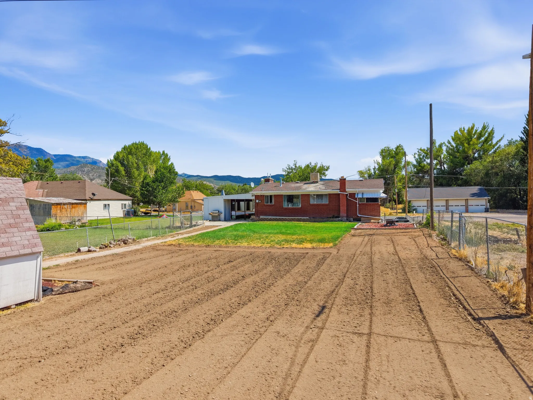 Expansive tilled garden space with established rows, bordered by a chain-link fence