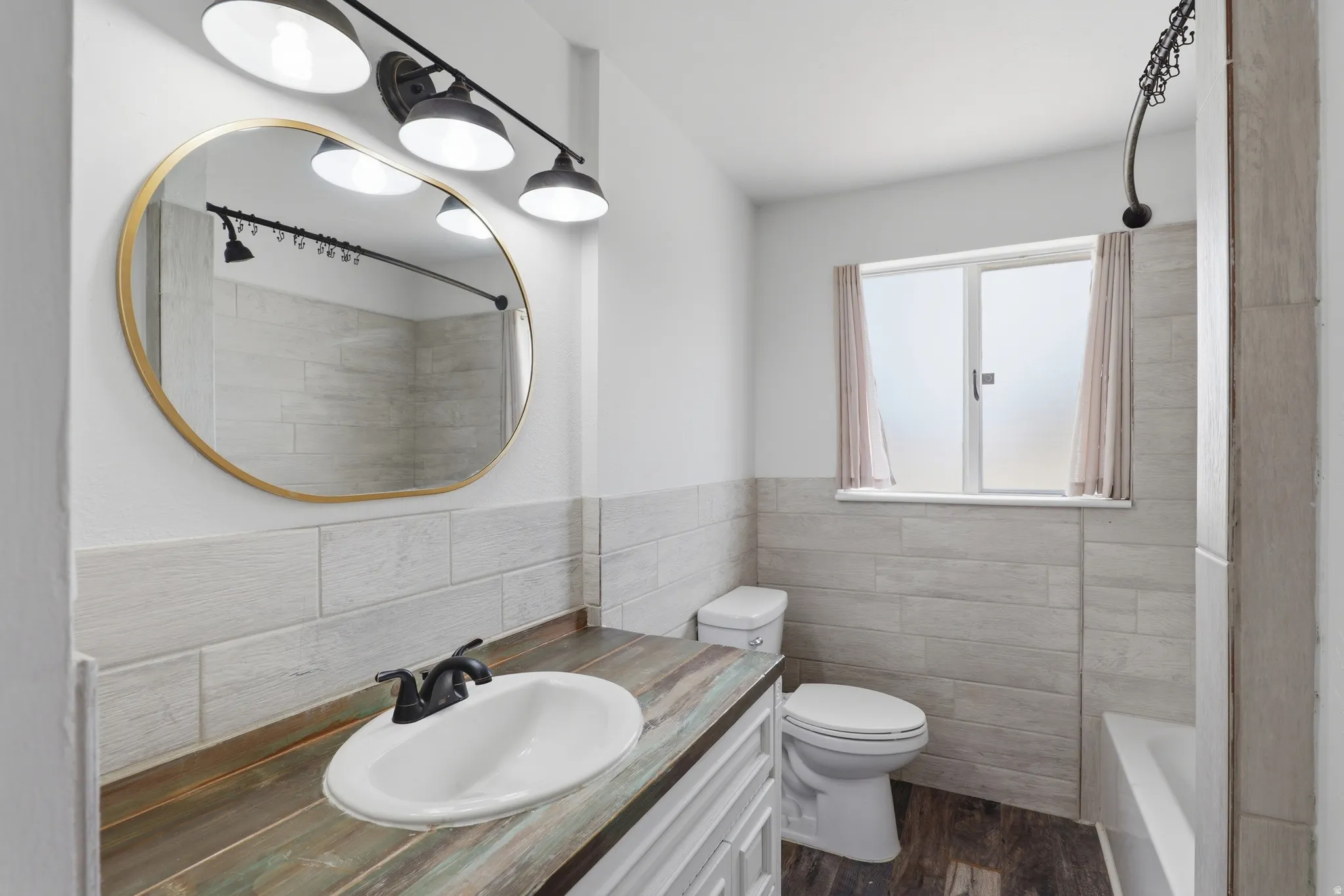 Bathroom vanity featuring a vessel sink with a matte black faucet, a gold-framed oval mirror, and a three-light fixture