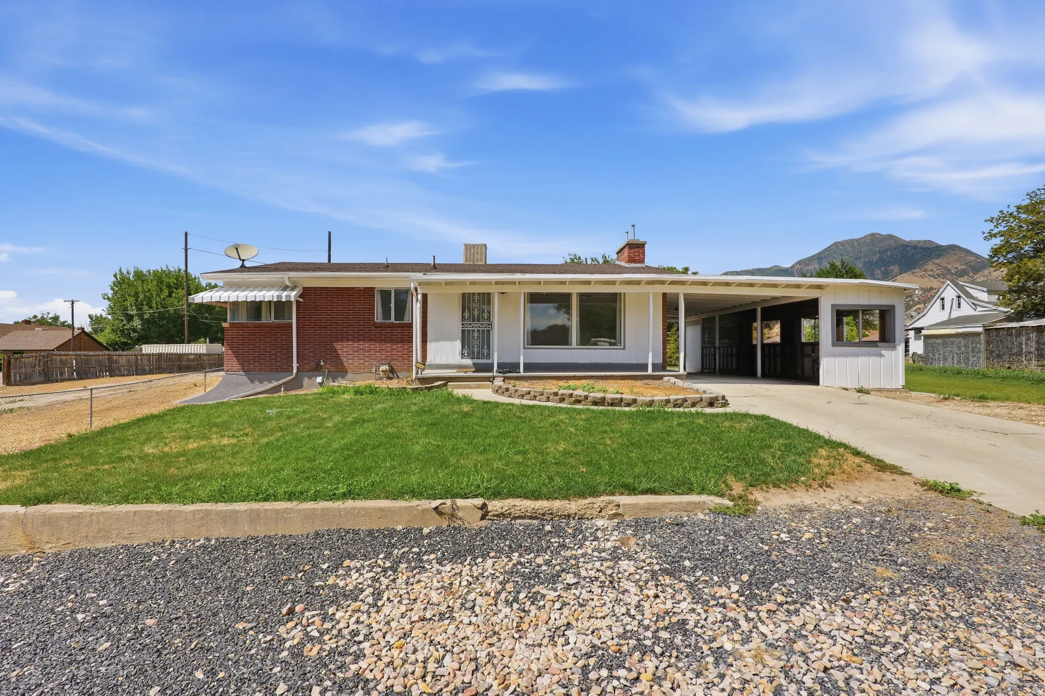 Brick and white siding exterior featuring a covered carport, front yard with a landscaped planter, and a prominent mountain backdrop