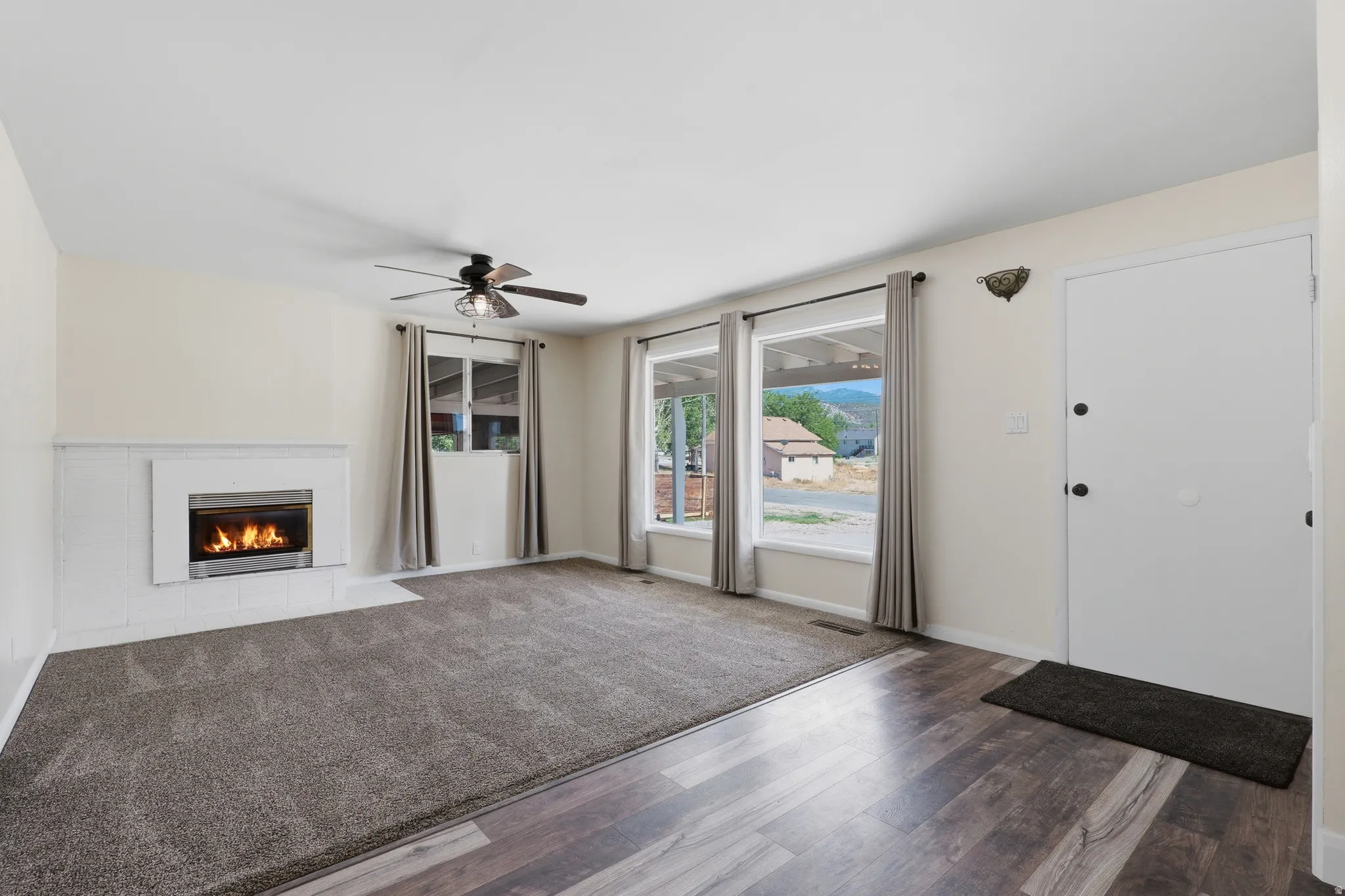 Spacious living area featuring a modern fireplace with a white tile surround, wood-finish flooring, broad windows, and a ceiling fan