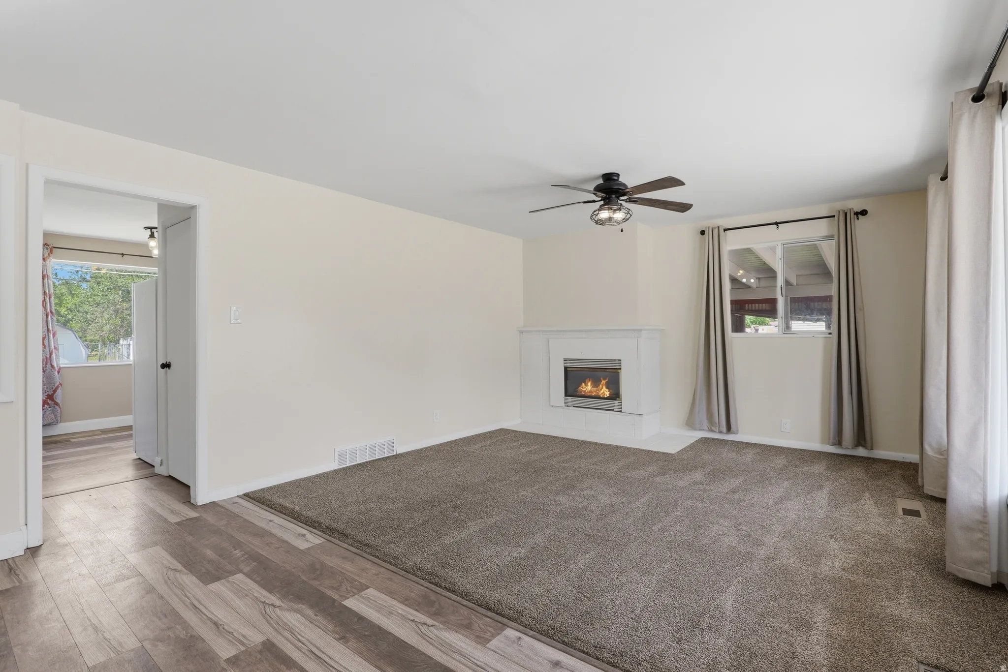 Living area featuring a white mantel fireplace with a stainless steel insert, wood-finish flooring, and a ceiling fan with light fixture