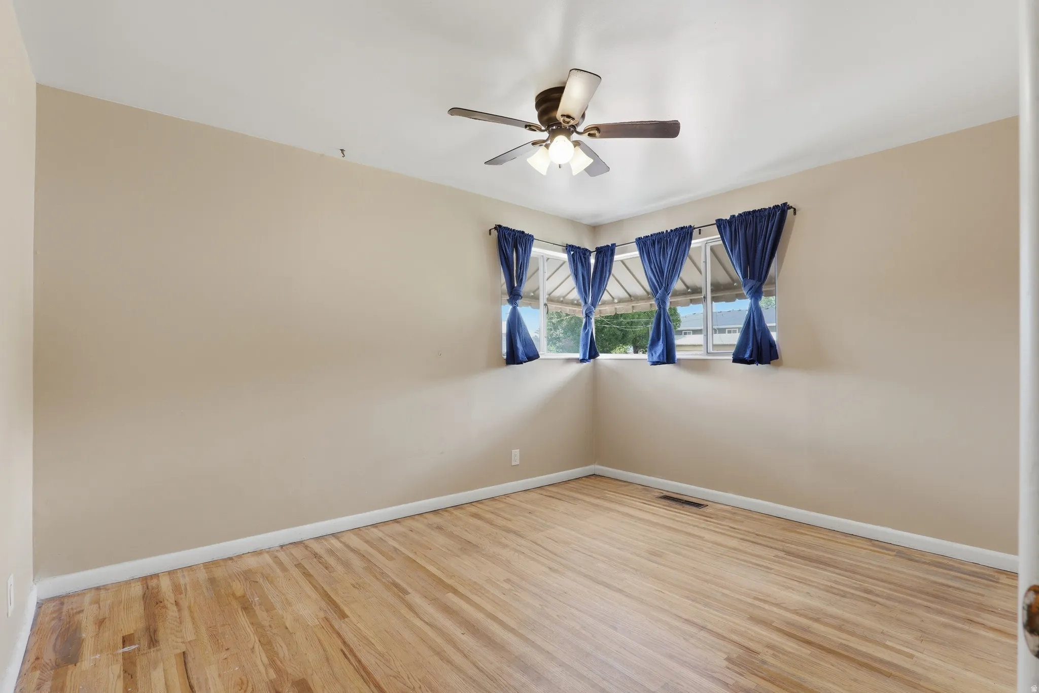 Room featuring wood-finish flooring, corner windows with trim, a ceiling fan with integrated lighting, and neutral wall tones