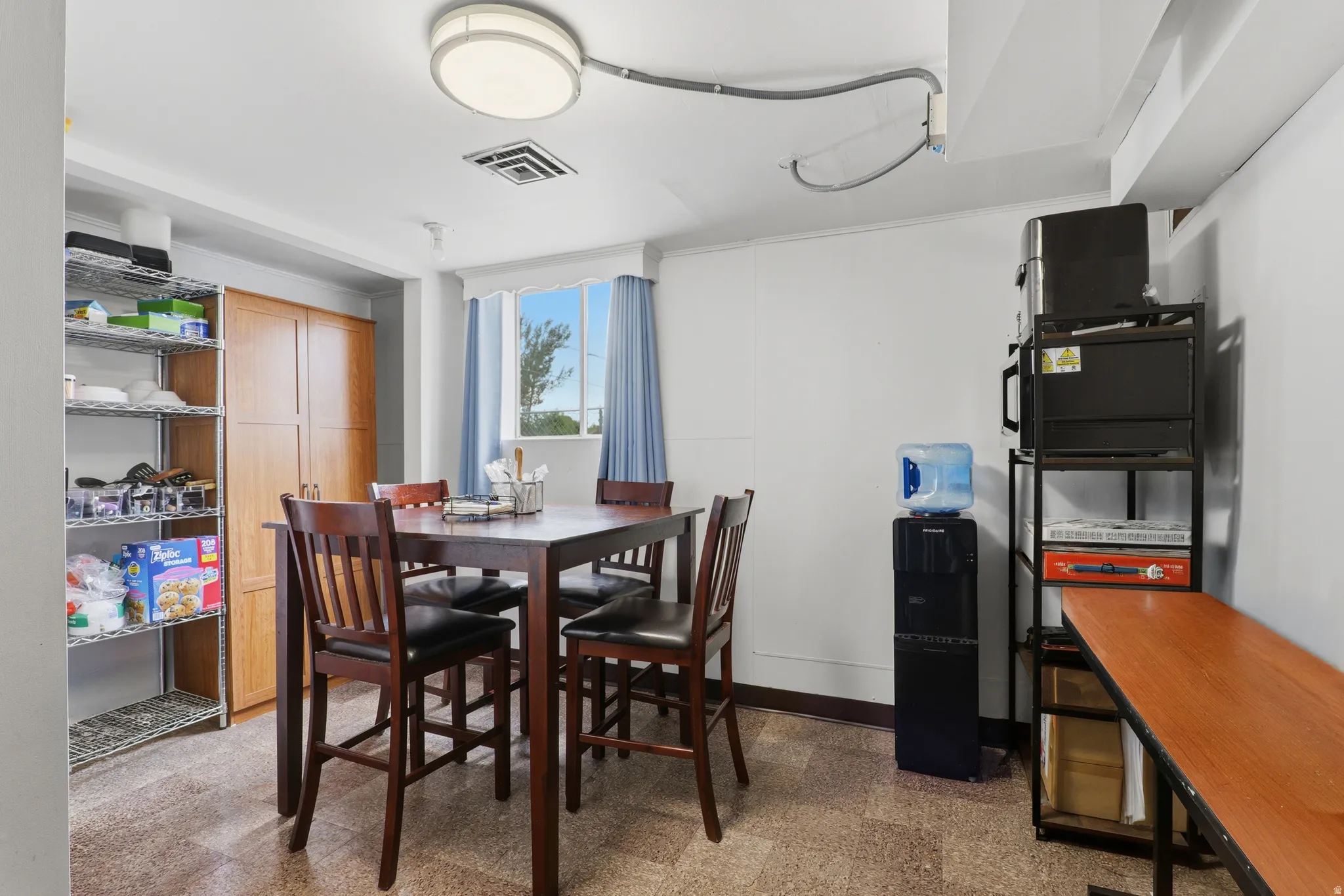 Dining area featuring a wood-finish table with four matching chairs, a bright window with blue drapes, and durable stone-look flooring