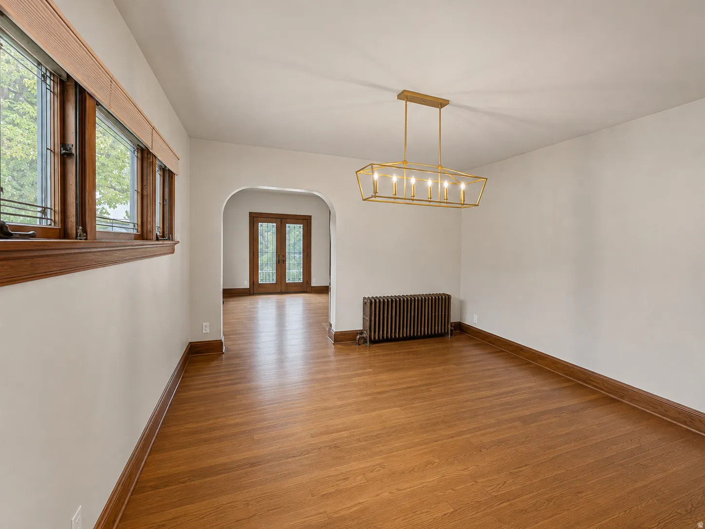 Hardwood flooring with wood trim throughout, an arched doorway, and a linear chandelier