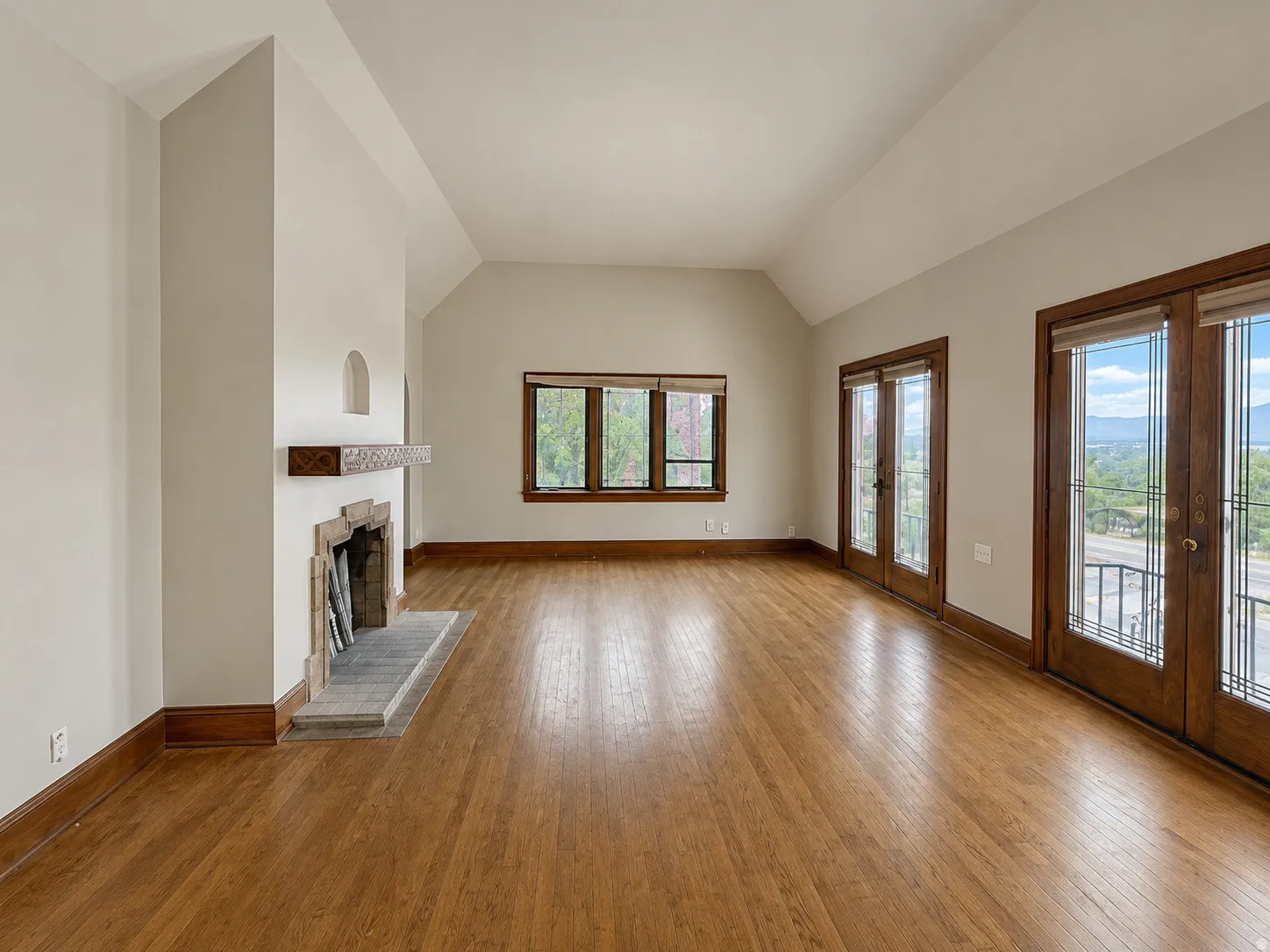 Spacious room featuring wood-finish flooring, a stone fireplace with a wood mantle, and multiple windows with wood frames