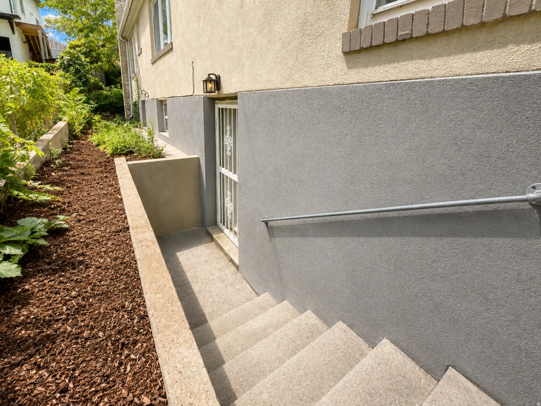 Exterior wall with stucco finish, concrete stairs, metal handrail, and a decorative security door