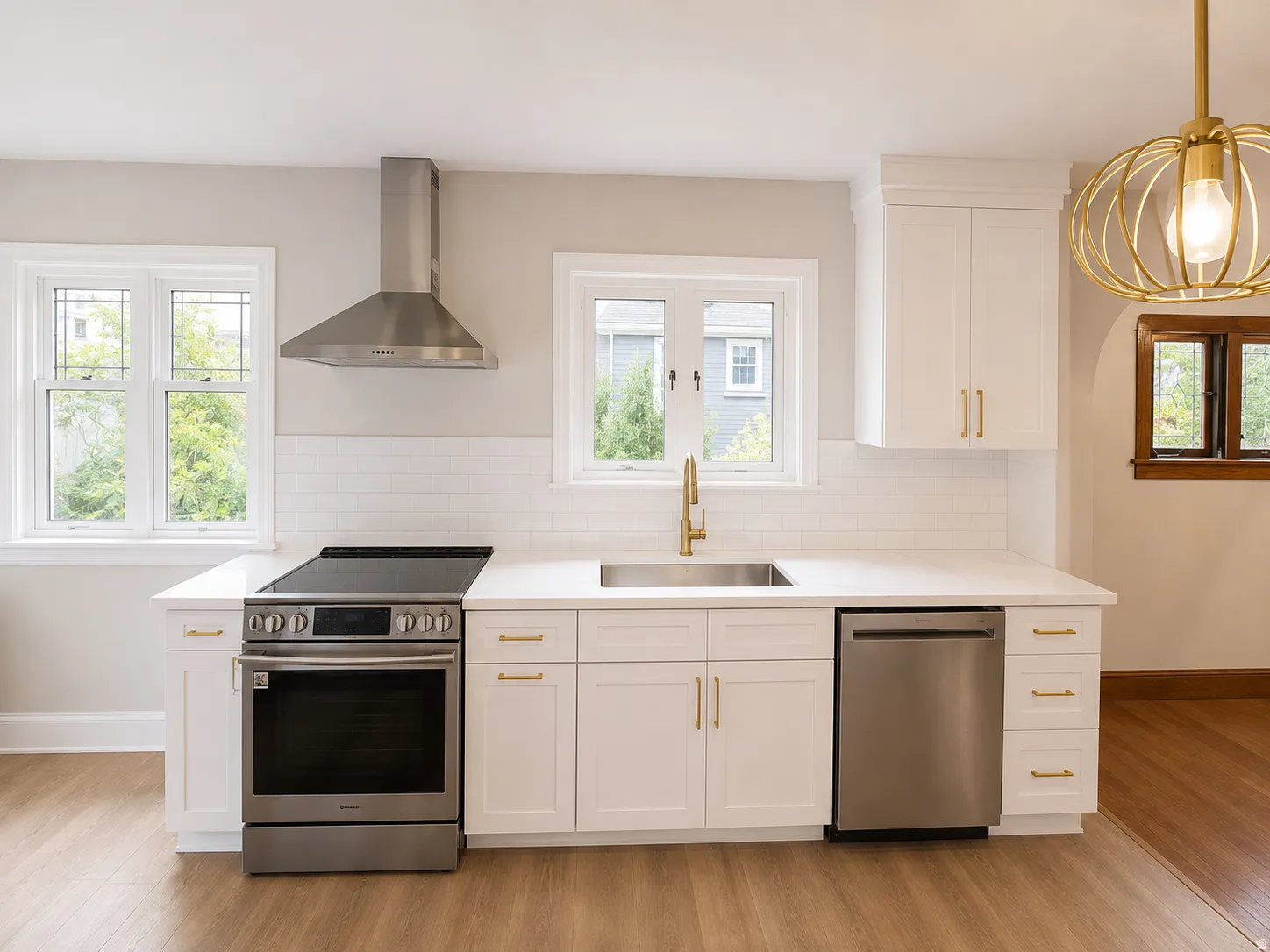 White cabinetry with gold-tone hardware, stainless steel appliances, solid surface countertops, a subway tile backsplash, and wood-finish flooring