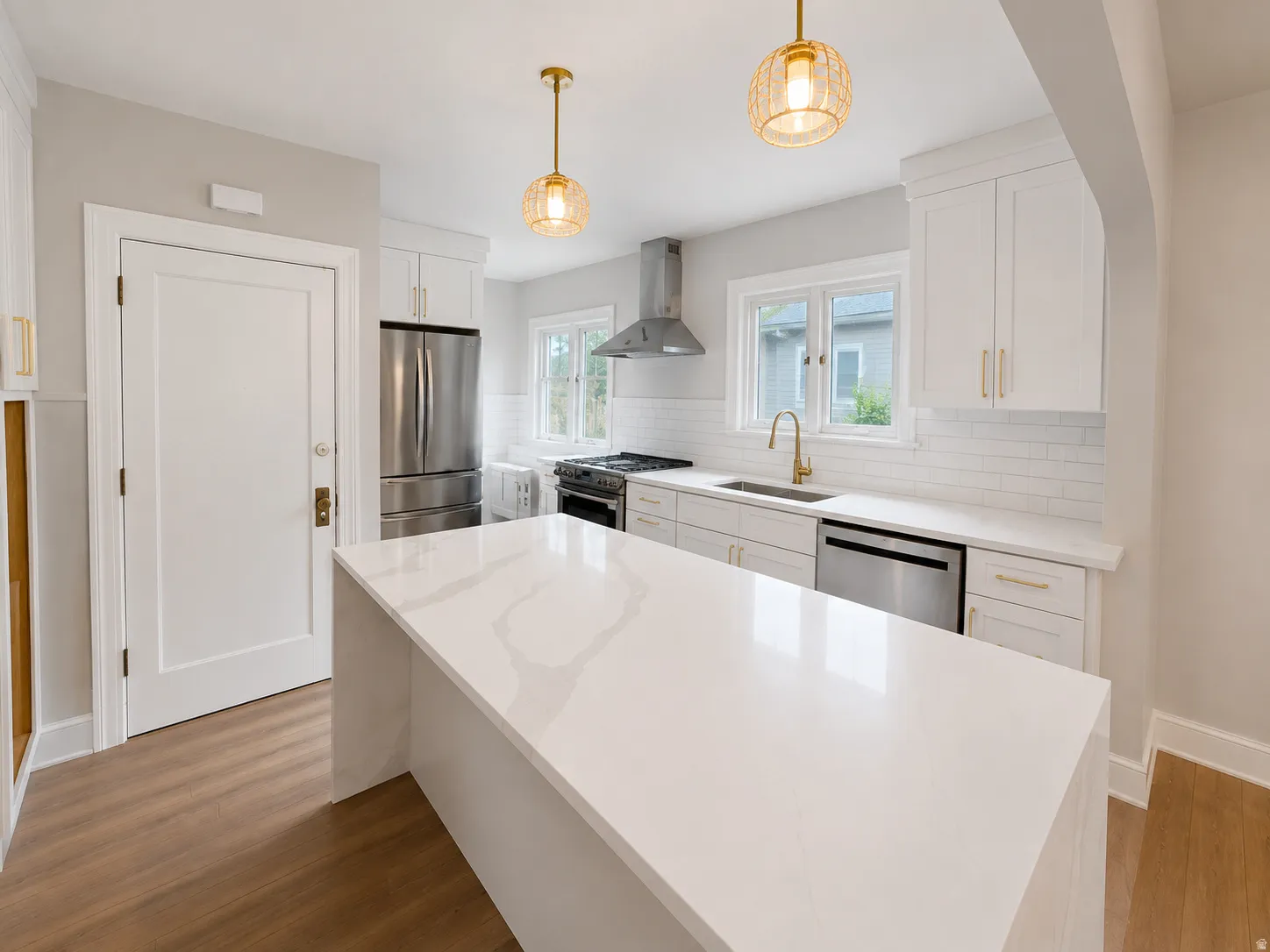 Kitchen featuring white cabinetry, stainless steel appliances, quartz countertops, subway tile backsplash, and wood-finish flooring