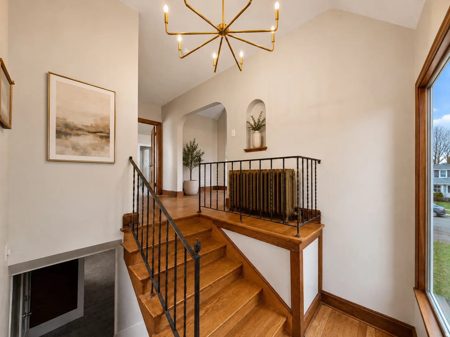 Hardwood flooring, wrought iron stair railing, arched doorway, recessed wall niche, and a contemporary chandelier