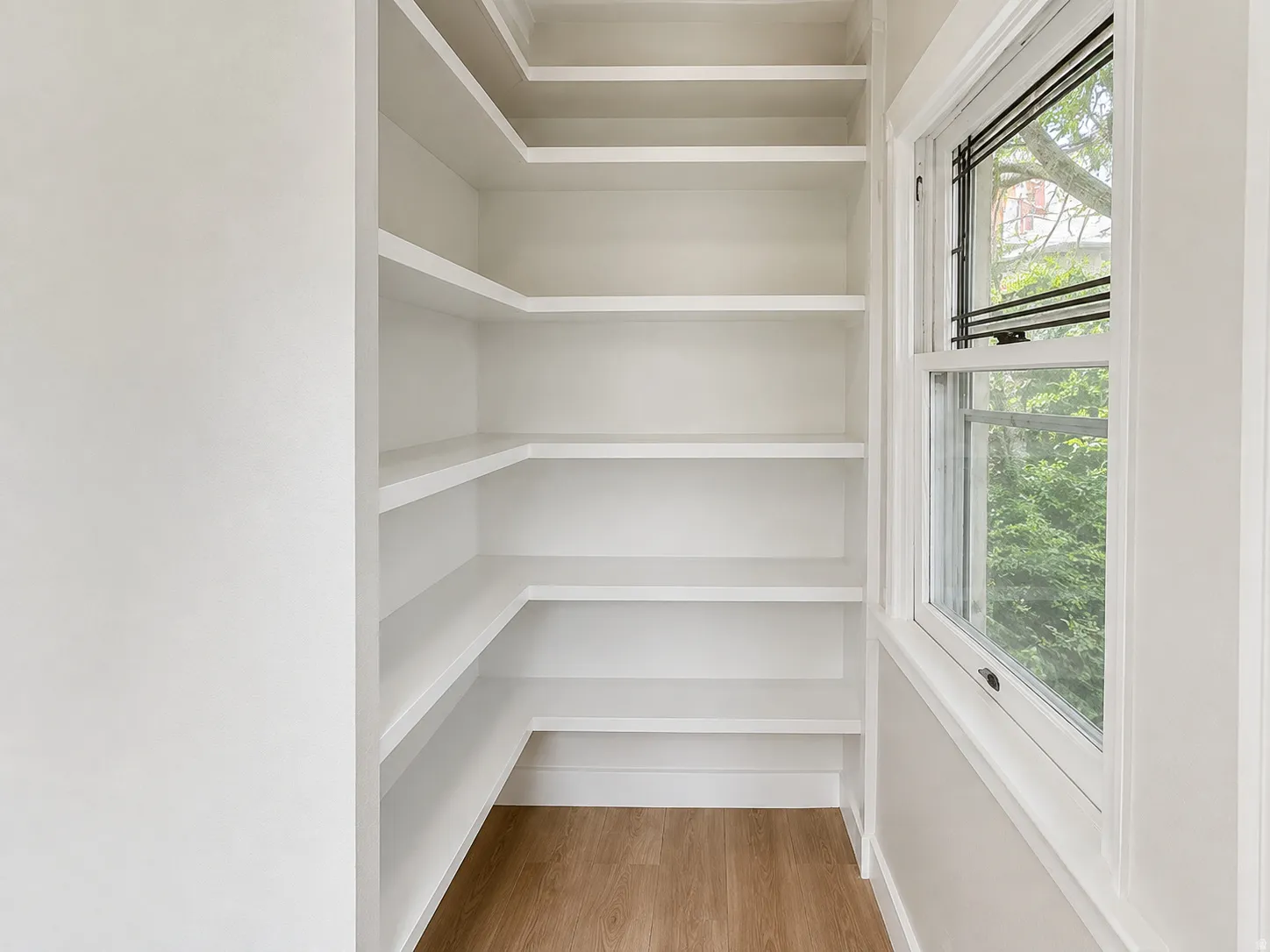 Built-in shelving unit with multiple shelves, single-hung window, and wood-finish flooring