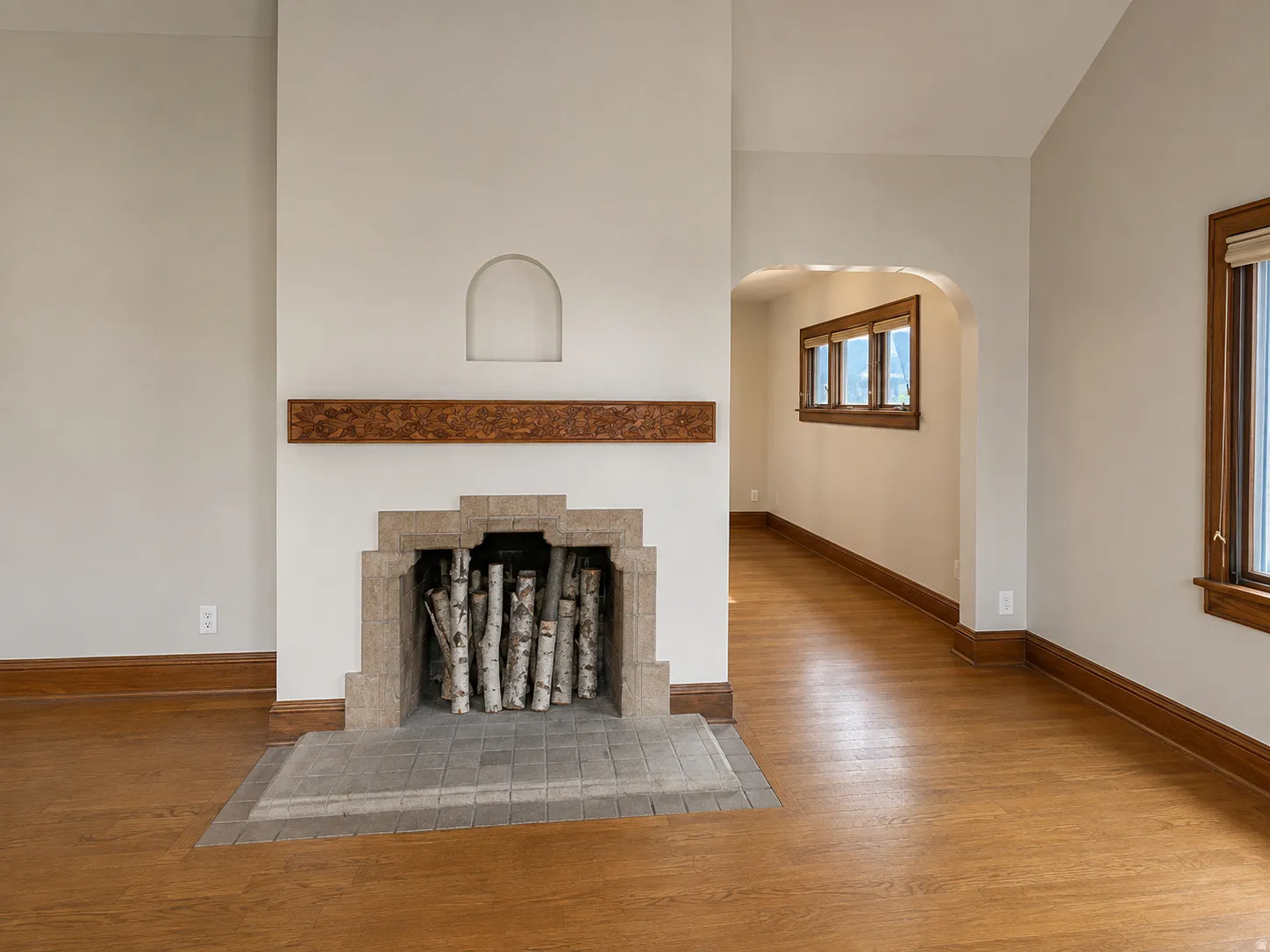 Stone fireplace with a carved wood mantel, arched wall niche, wood-finish flooring, and wood trim details
