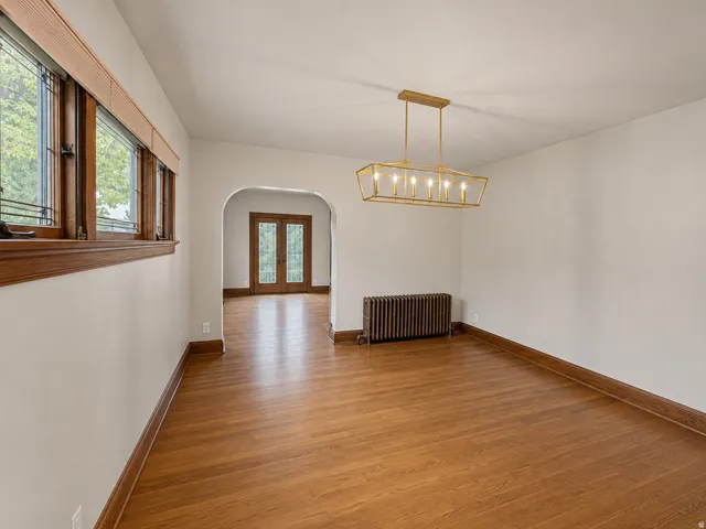 Hardwood flooring with wood trim throughout, an arched doorway, and a linear chandelier