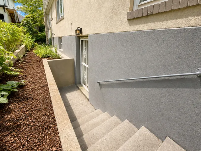 Exterior wall with stucco finish, concrete stairs, metal handrail, and a decorative security door