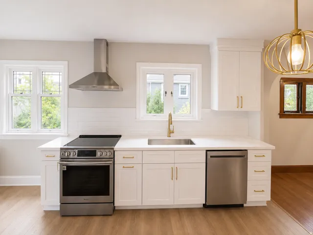 White cabinetry with gold-tone hardware, stainless steel appliances, solid surface countertops, a subway tile backsplash, and wood-finish flooring