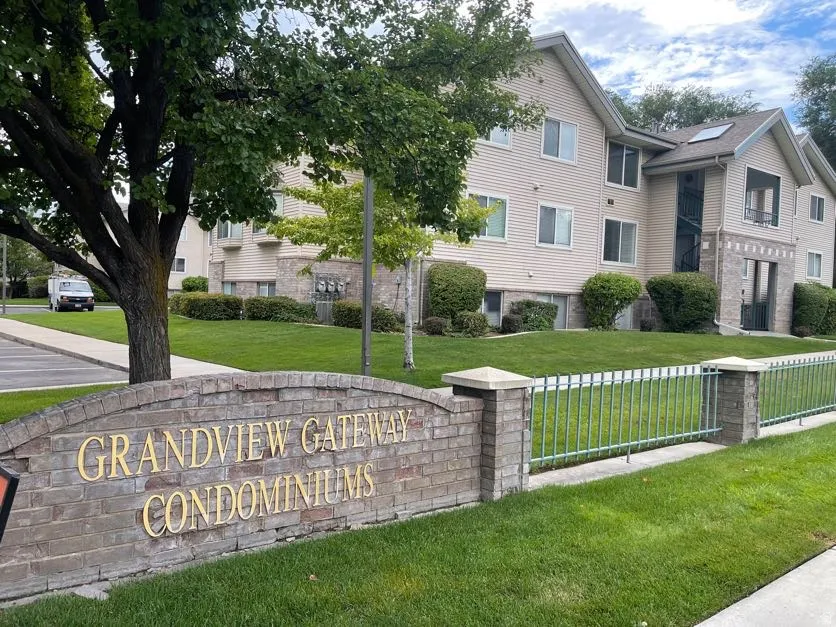 "Grandview Gateway Condominiums" signage featuring brick and stone accents, complemented by a metal fence and manicured lawn