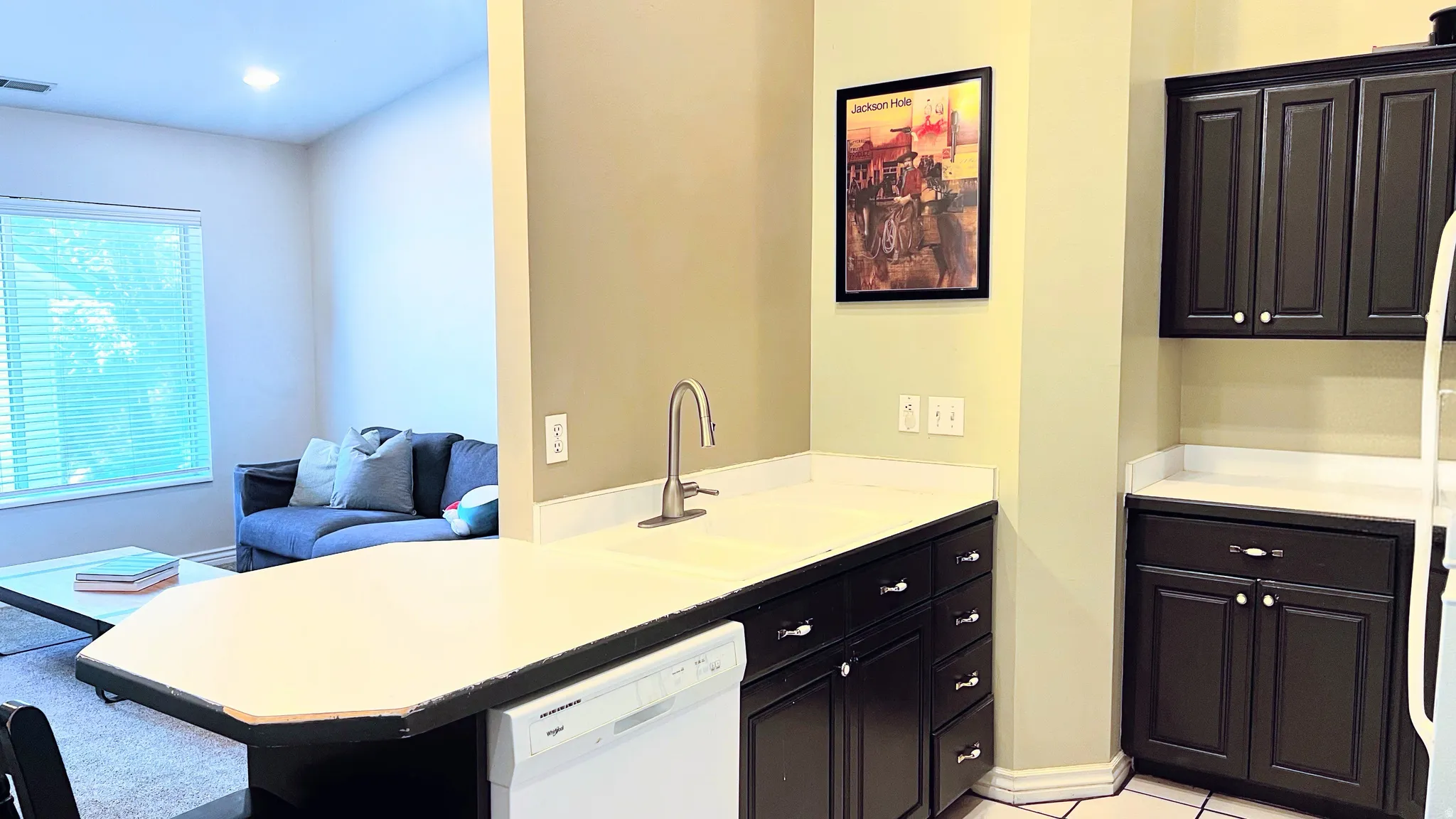 Kitchen featuring dark cabinetry, light-colored countertops, a stainless steel faucet, and an integrated dishwasher