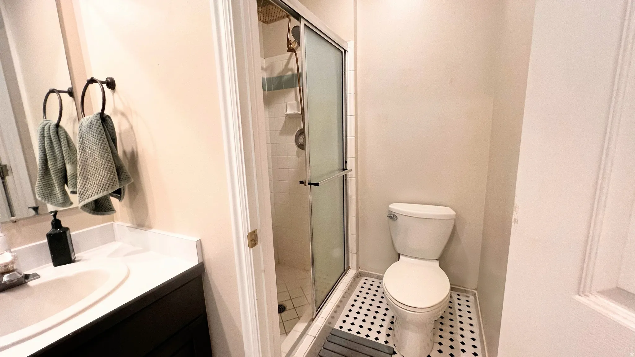 Master Bathroom featuring a glass-enclosed shower, white subway tile shower surround, black and white mosaic tile flooring, a dark wood-finish vanity with a white countertop, and a white porcelain sink