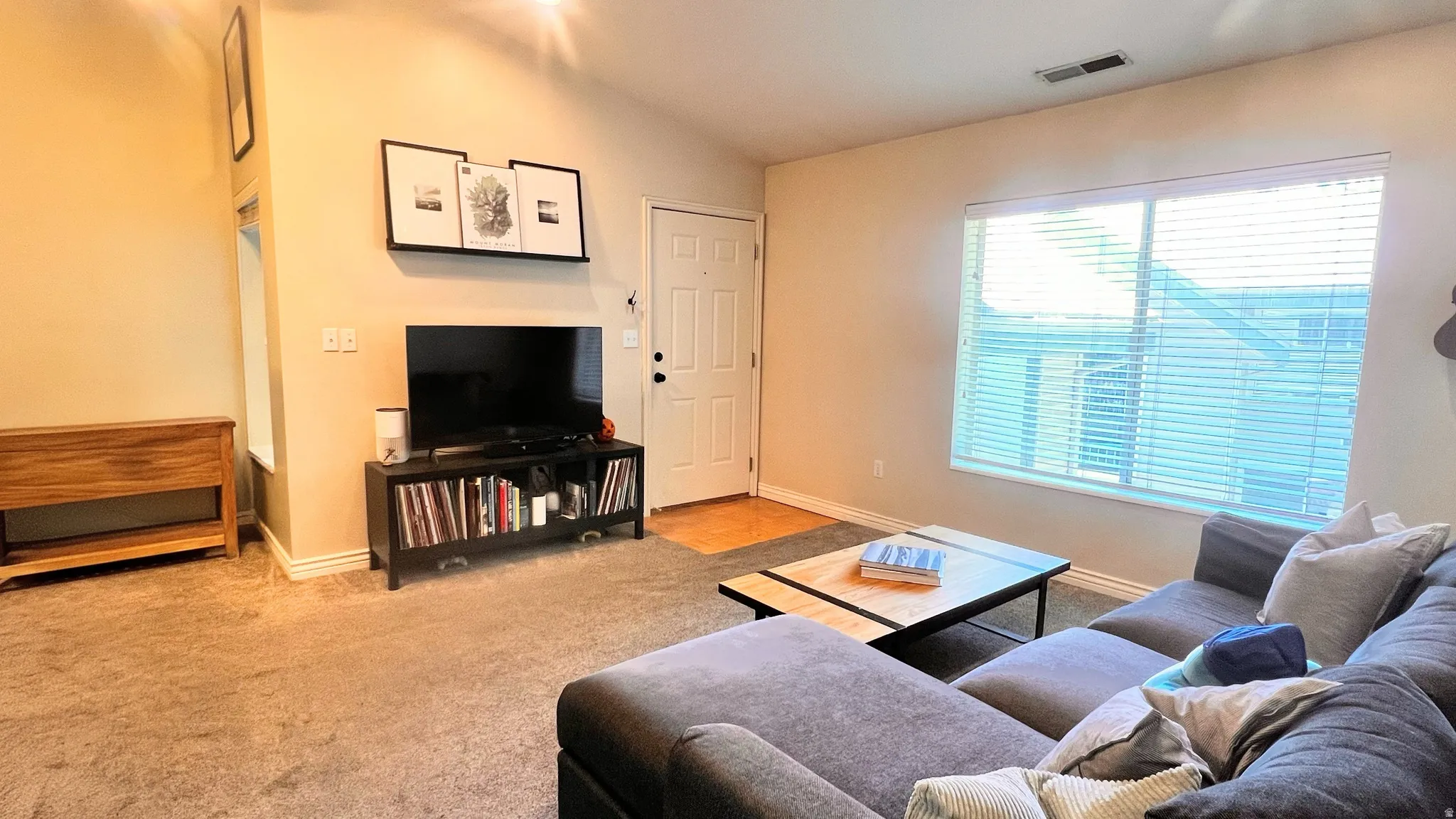 Open-concept living area featuring a vaulted ceiling and neutral-toned carpeting