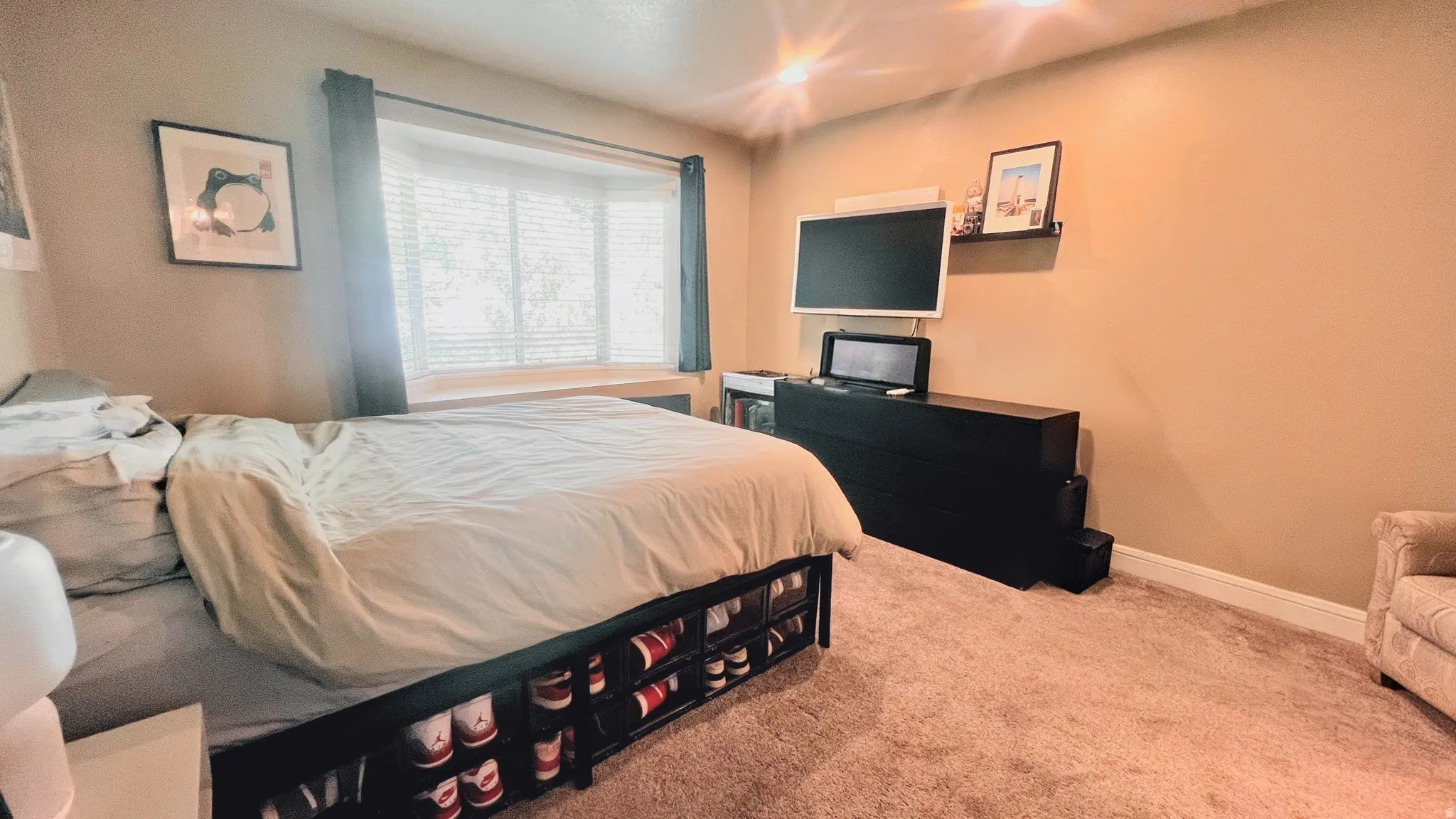 Primary bedroom, Bay window with blinds, light tan walls, and carpet flooring