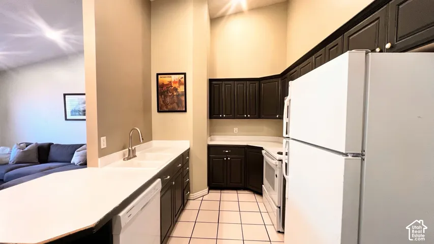 Kitchen featuring dark cabinetry, light countertops, and white appliances