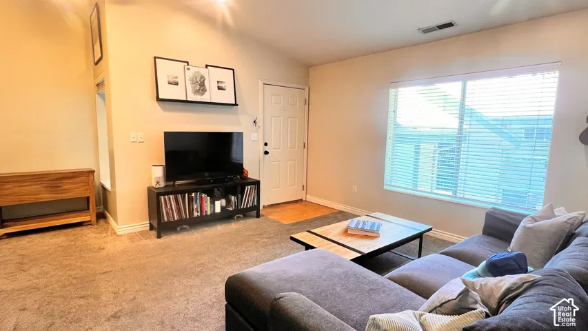 Open-concept living area featuring a vaulted ceiling and neutral-toned carpeting