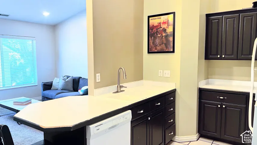 Kitchen featuring dark cabinetry, light-colored countertops, a stainless steel faucet, and an integrated dishwasher