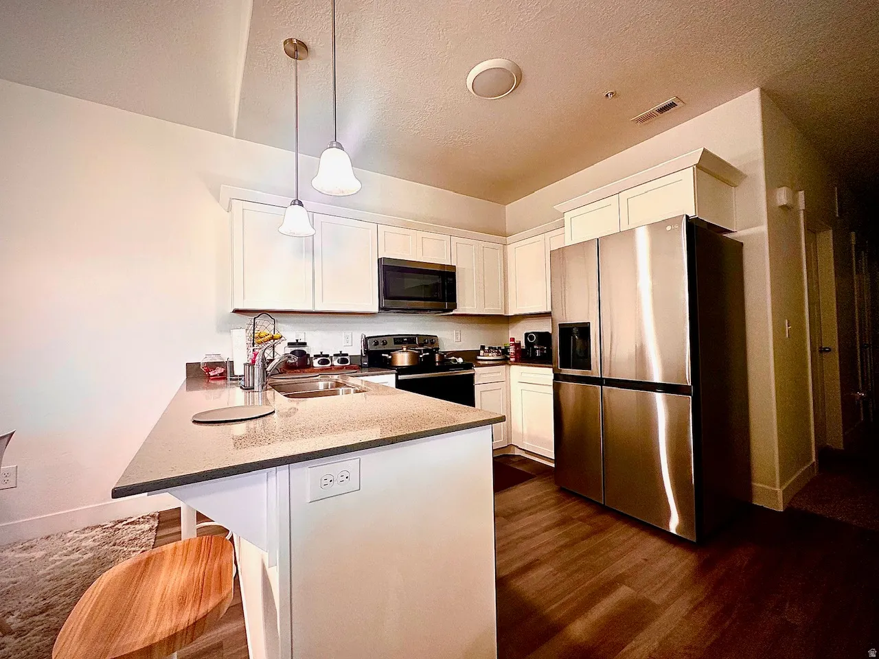 Modern kitchen featuring white cabinetry, stainless steel appliances, wood-finish flooring, a double basin sink, and pendant lighting