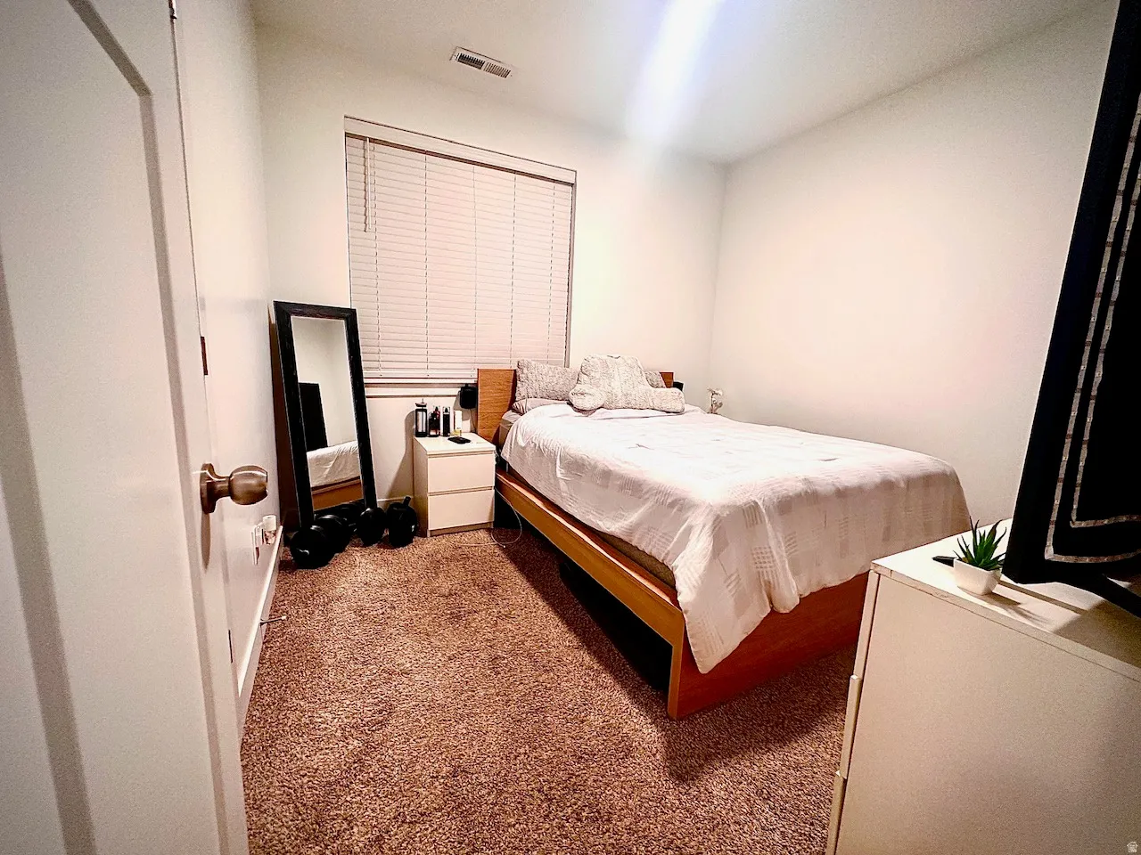 Carpeted room featuring a single window with blinds and a ceiling vent