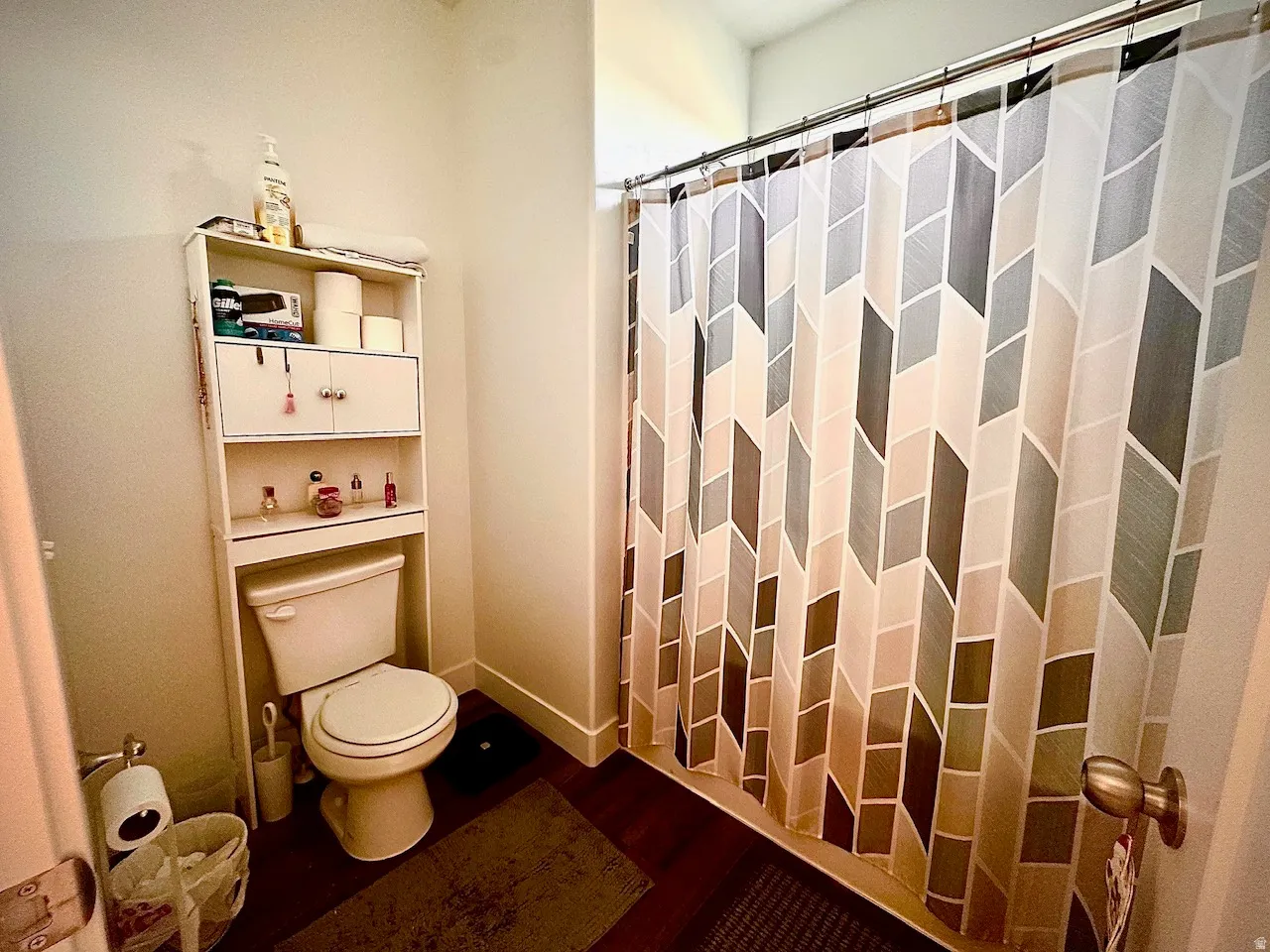 Full bathroom featuring a shower with a geometric pattern curtain, a toilet, and an over-the-toilet storage unit