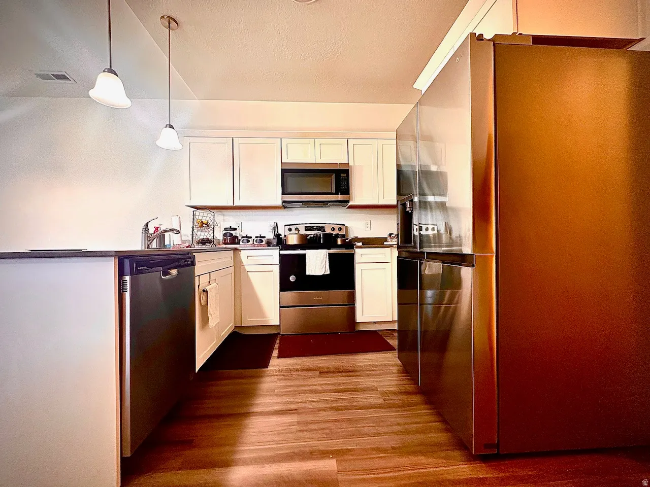 Kitchen featuring wood-finish flooring, white cabinetry, stainless steel appliances, and pendant lighting
