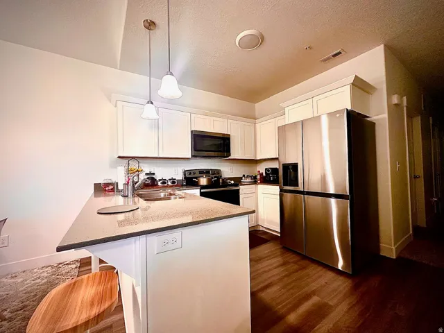 Modern kitchen featuring white cabinetry, stainless steel appliances, wood-finish flooring, a double basin sink, and pendant lighting